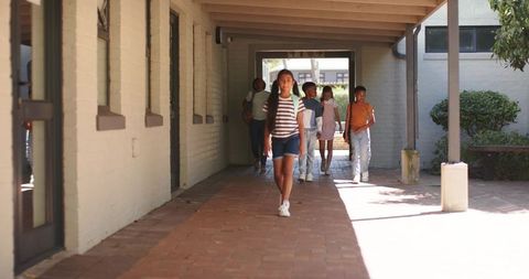 Diverse teens walking through campus arcade toward sunlit courtyard with backpacks
