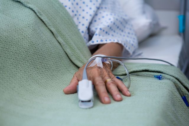 Close-up of senior patient hand with saline on bed in hospital