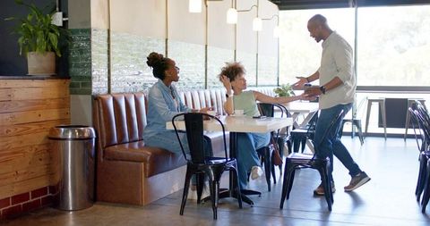 Friends chatting and laughing at sunlit cafe booth over coffee, casual urban social scene