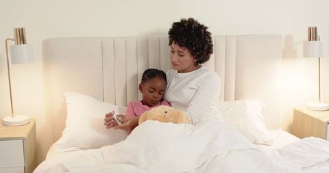 Mother Comforting Child in Bed Holding Thermometer Reflecting Warmth and Care