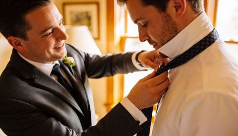 Groomsman adjusting groom's tie during wedding preparation with boutonniere