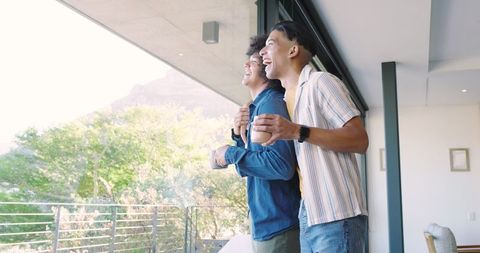 Two Friends Enjoying Scenic Balcony View Holding Coffee Mugs
