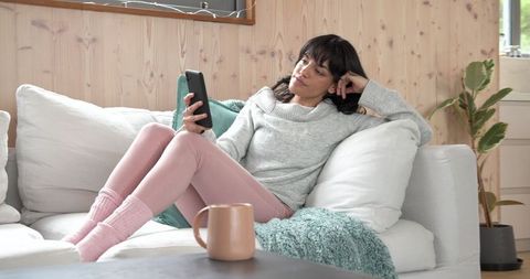 Woman Relaxing on Cozy Sofa with Smartphone in Tranquil Living Room
