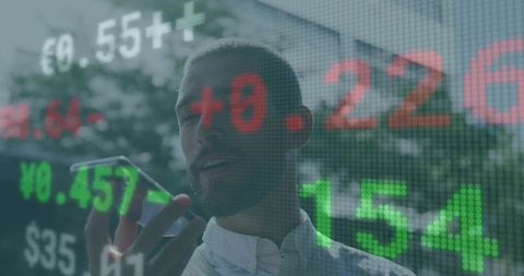 Man speaking on smartphone while holding device with stock market data overlay on urban facade