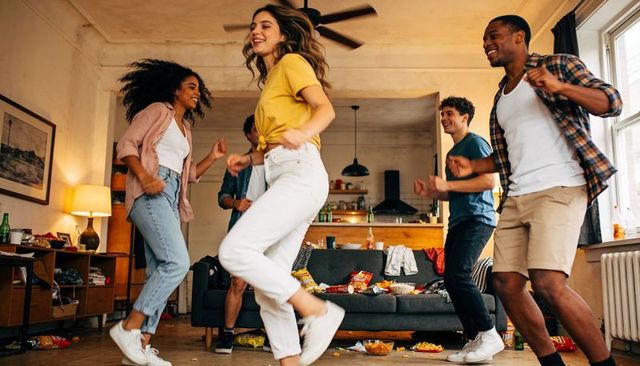 Young friends dancing and laughing in lively apartment living room during casual house party