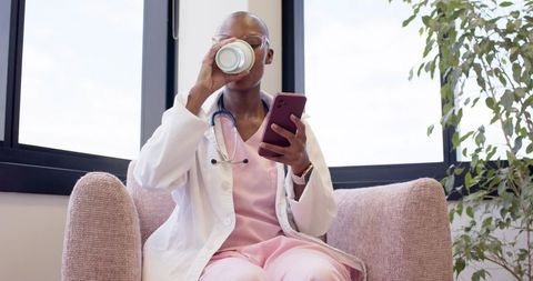 Medical provider drinking coffee and checking phone in clinic lounge with stethoscope