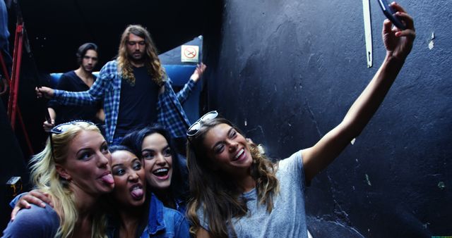 Group of young people having fun taking selfie in a dimly lit interior. Ideal for content related to friendship, nightlife, fun activities, social media trends, youth culture, and spontaneous moments.