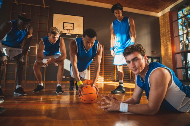 Diverse male basketball team watching and exercising in sunny indoor gym. basketball, team sports training at an indoor court.