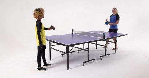 Female friends enthusiastically playing table tennis indoors