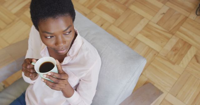 Happy african american woman sitting on armchair in living room, drinking coffee. domestic life, spending time at home.