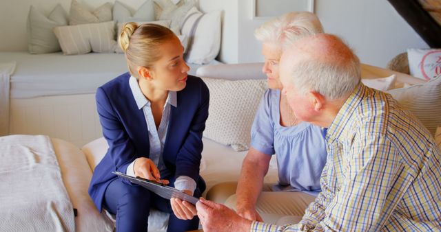 A young financial advisor meeting with a senior couple in a cozy home setting. They are engaging in a serious discussion, with the advisor showing documents on a tablet. Ideal for use in content related to financial planning, retirement advice, family financial services, senior care discussions, or business consultancy advertising.