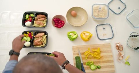 Meal prep with grilled chicken, penne pasta and fresh veggies on white countertop