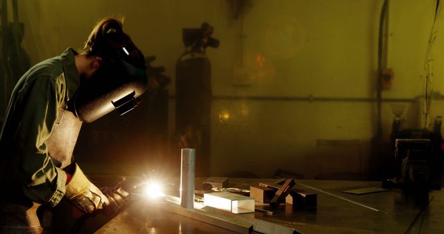 Welder working with industrial tool in workshop, creating sparks. Wearing protective mask and gloves for safety. Ideal for illustrating concepts of industrial labor, engineering, manufacturing processes, and workplace safety. Suitable for articles, advertisements, and training materials related to welding and other metalwork tasks.