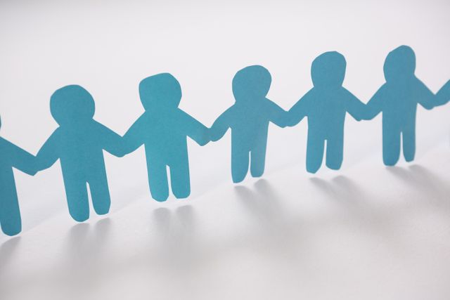 This image of blue paper cut-out figures holding hands symbolizes teamwork, unity, and collaboration. It is ideal for use in presentations, websites, and promotional materials related to community building, support groups, and team activities. The minimalist design and white background make it versatile for various contexts, including educational and corporate settings.