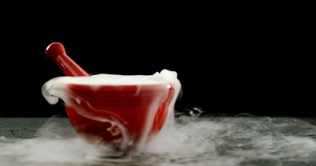 Mystical red mortar and pestle with white smoke curling around it on a black background. Perfect for use in content related to chemistry experiments, culinary processes, or magical themes. Visually striking for educational, healthcare, or advertisement purposes.