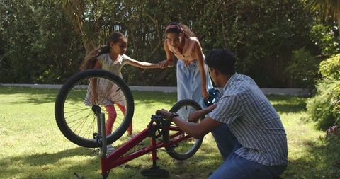 family collaborating to fix bicycle in sunny backyard - Download Free Stock Images Pikwizard.com