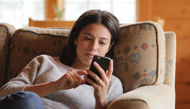 Woman relaxing on cozy sofa while scrolling smartphone, casual home lifestyle moment