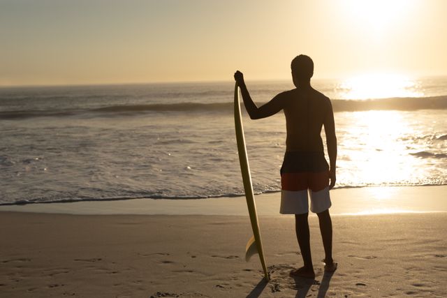 Rear view of man standing with surfboard on the beach