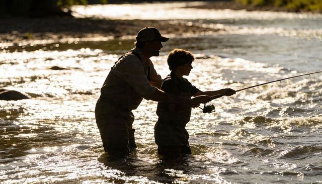 Guardian guiding child casting spinning fishing rod in sunlit river while wading