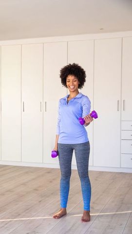African american woman lifting dumbbells at home smiling minimalist full body workout