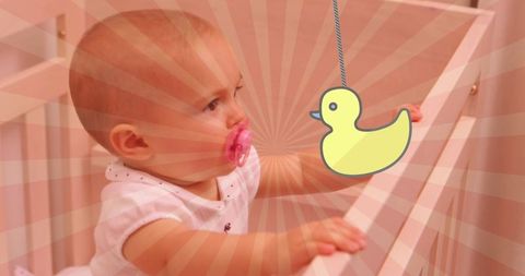 Happy caucasian baby with cartoon duck in crib