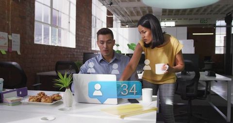 Coworkers collaborating over laptop reviewing social notification in modern industrial office