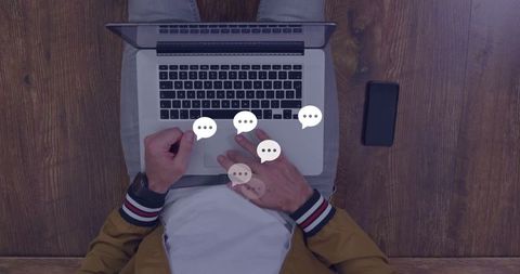 Man Typing on Laptop with Chat Icons and Phone on Desk