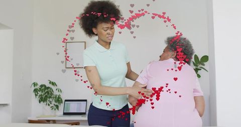 Caregiver steadying senior turning in home with laptop and heart graphics, supportive care