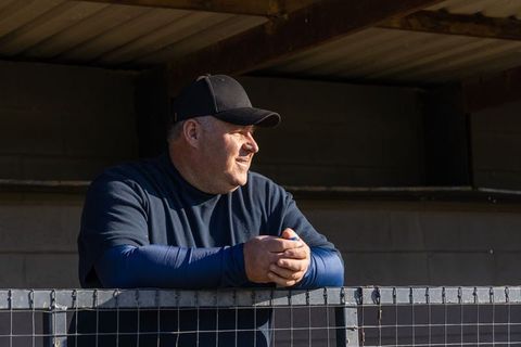 Mature man leaning on railing watching game under corrugated roof wearing black cap