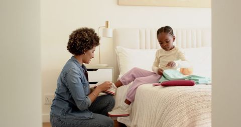 Mother Assisting Daughter by Bedside Tying Sneakers