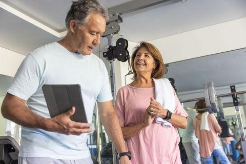 Mature couple training together in gym using tablet and smartwatch for active retirement fitness