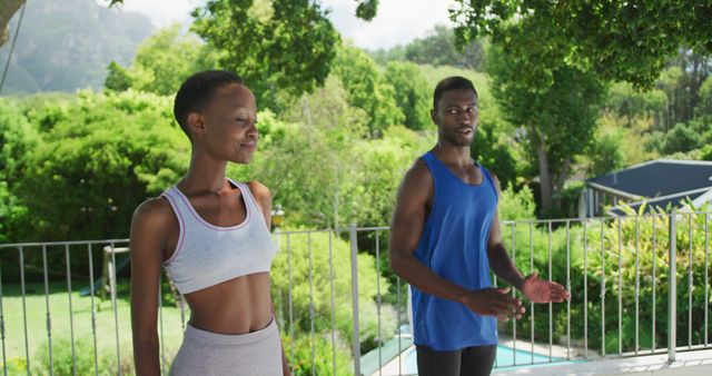 African american couple practicing yoga exercising on sunny garden terrace. staying at home in isolation during quarantine lockdown.