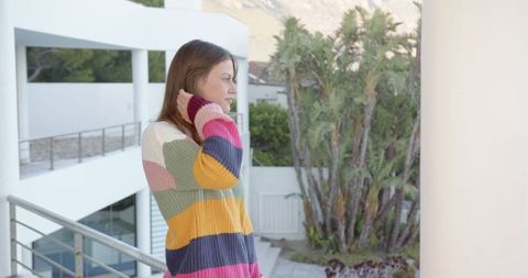 Woman in Colorful Striped Sweater Enjoying Balcony View