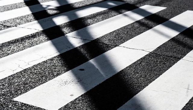 Crosswalk stripes revealing worn paint and diagonal shadows on textured urban asphalt