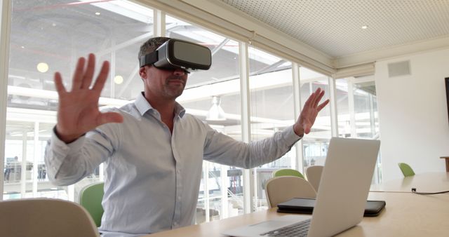 Businessman using VR headset while working in modern office, showcasing the integration of virtual reality technology in professional settings. Useful for themes around innovative workflows, high-tech office environments, and blending virtual reality with daily tasks.