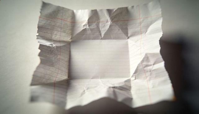Crumpled wide-ruled notebook paper with torn edges and blank square center on desk