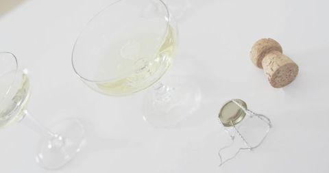 Minimal champagne coupe with sparkling bubbles, cork and wire muselet on white high-key backdrop