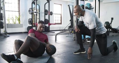 Senior Trainer Guiding Man Performing Russian Twist in Gym