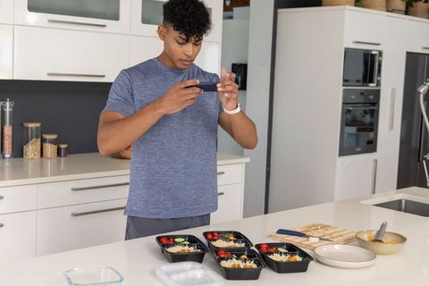 African american man photographing meal-prep containers on modern minimalist kitchen island