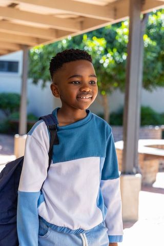 Smiling schoolboy walking with backpack through sunlit school courtyard