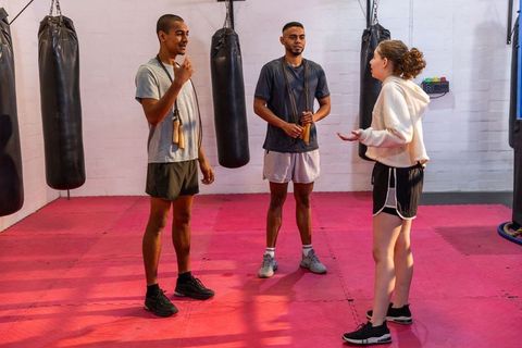 Diverse fitness trio training with jump ropes in boxing gym on red mats, teamwork focus