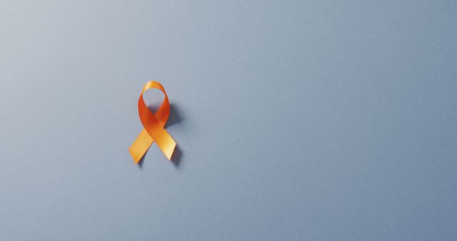 An orange ribbon placed on a light blue background symbolizes awareness and support for a specific cause or health condition. This image is perfect for health campaigns, social media posts, or promotional materials for charity events and awareness movements.