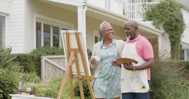 Happy senior african american couple painting picture in garden, drinking coffee and talking. Retirement, togetherness, creativity, hobbies and senior lifestyle, unaltered.
