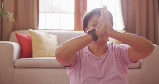 Senior woman wearing casual attire practicing a yoga pose in her cozy living room. Perfect for illustrating healthy lifestyle choices, mindfulness practices, and at-home fitness routines. Useful for articles and blog posts on mental health, physical wellbeing, and holistic approaches to maintaining a balanced life.