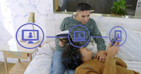 Couple lounging on bed reading and scrolling with digital connectivity overlay