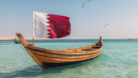 Traditional wooden qatar dhow with qatari flag floating on turquoise arabian gulf waters
