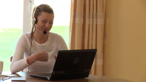 Woman Laughing with Headset Using Laptop at Home