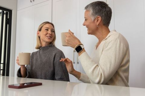 Senior and adult women chatting over coffee at modern kitchen island, cozy home conversation