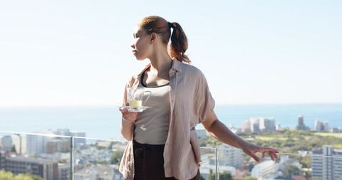 Woman enjoying morning coffee on coastal rooftop balcony overlooking city and ocean