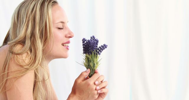 A young Caucasian woman enjoys the fragrance of fresh lavender flowers, with copy space. Her expression conveys a sense of relaxation and appreciation for the simple pleasures in life.